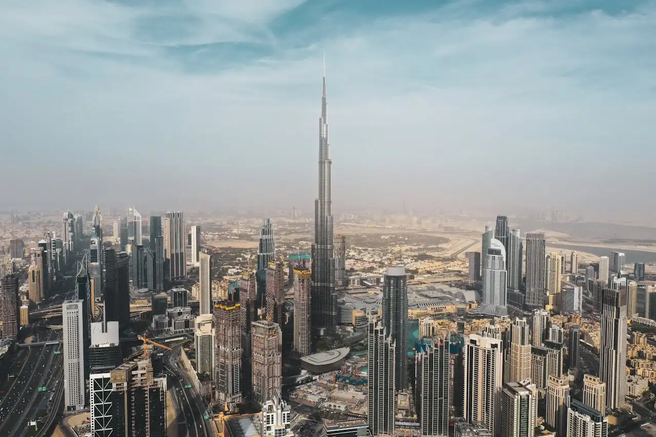 Aerial view of a bustling cityscape with modern skyscrapers densely packed together. The tallest building, prominently standing in the center, towers above the rest. The sky is partly cloudy, providing a backdrop to the impressive urban skyline—captured perfectly in a Dubai photoshoot with a personal travel photographer.